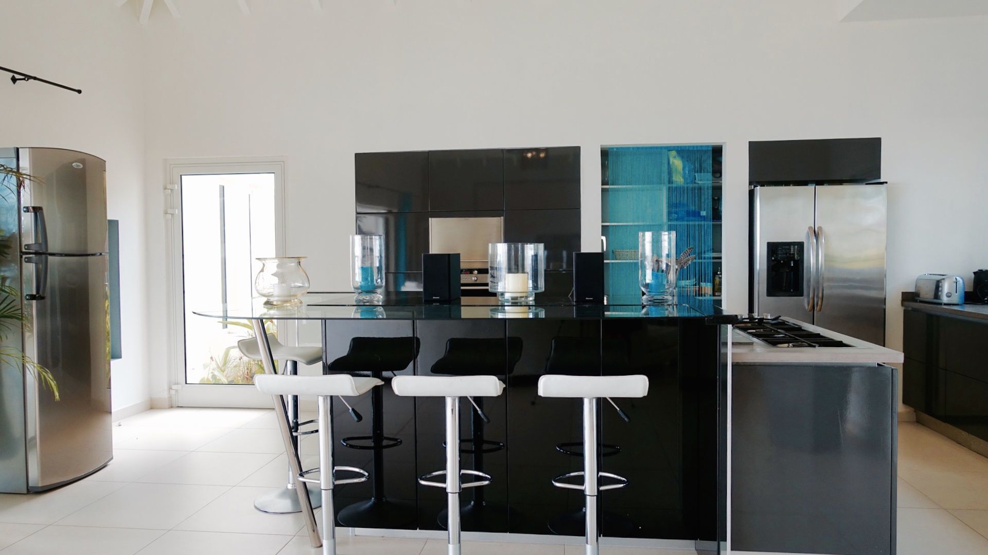 A modern kitchen with a central island, black bar stools, stainless steel appliances, and a glass backsplash.
