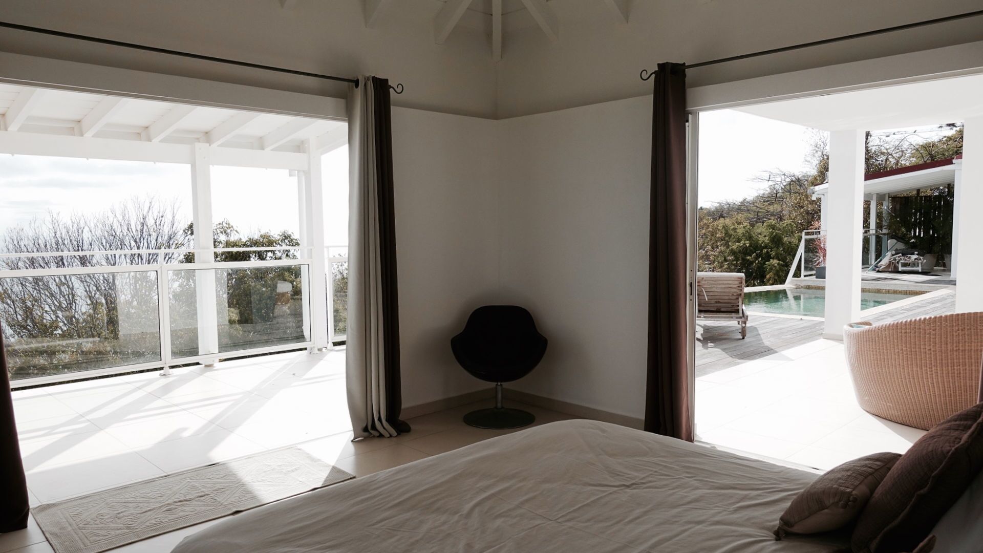 Ein Schlafzimmer mit großem Bett, Blick auf einen Pool und Sitzgelegenheit im Freien, und einem modernen Design.