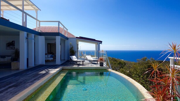 Une maison moderne dotée d’une piscine, d’un patio couvert et offrant une vue sur l’océan.