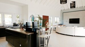 Une cuisine moderne dotée d’un îlot central, d’un coin repas aux couleurs claires et d’un téléviseur à écran plat fixé au mur.