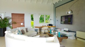 Un salon moderne avec un canapé blanc, un mur d’accent en bois, une table basse en verre et une grande fenêtre donnant sur un paysage verdoyant.