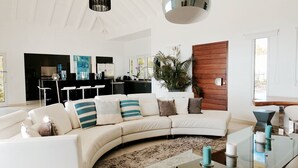 Un salon moderne avec un canapé blanc aux lignes courbes, une table basse en verre et un mur d’accent en bois.