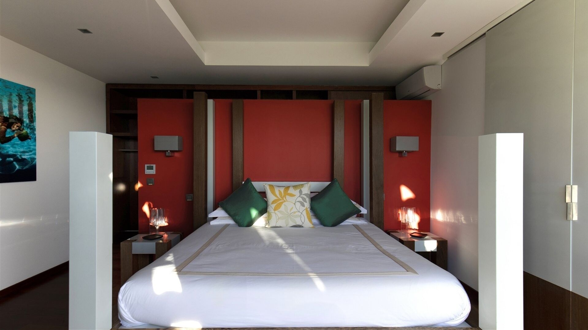 A modern hotel room with a large bed, red accent walls, and two bedside tables with lamps.