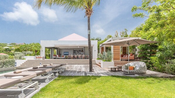 Une maison moderne dotée d’un patio couvert, d’un espace salon extérieur et d’une piscine.