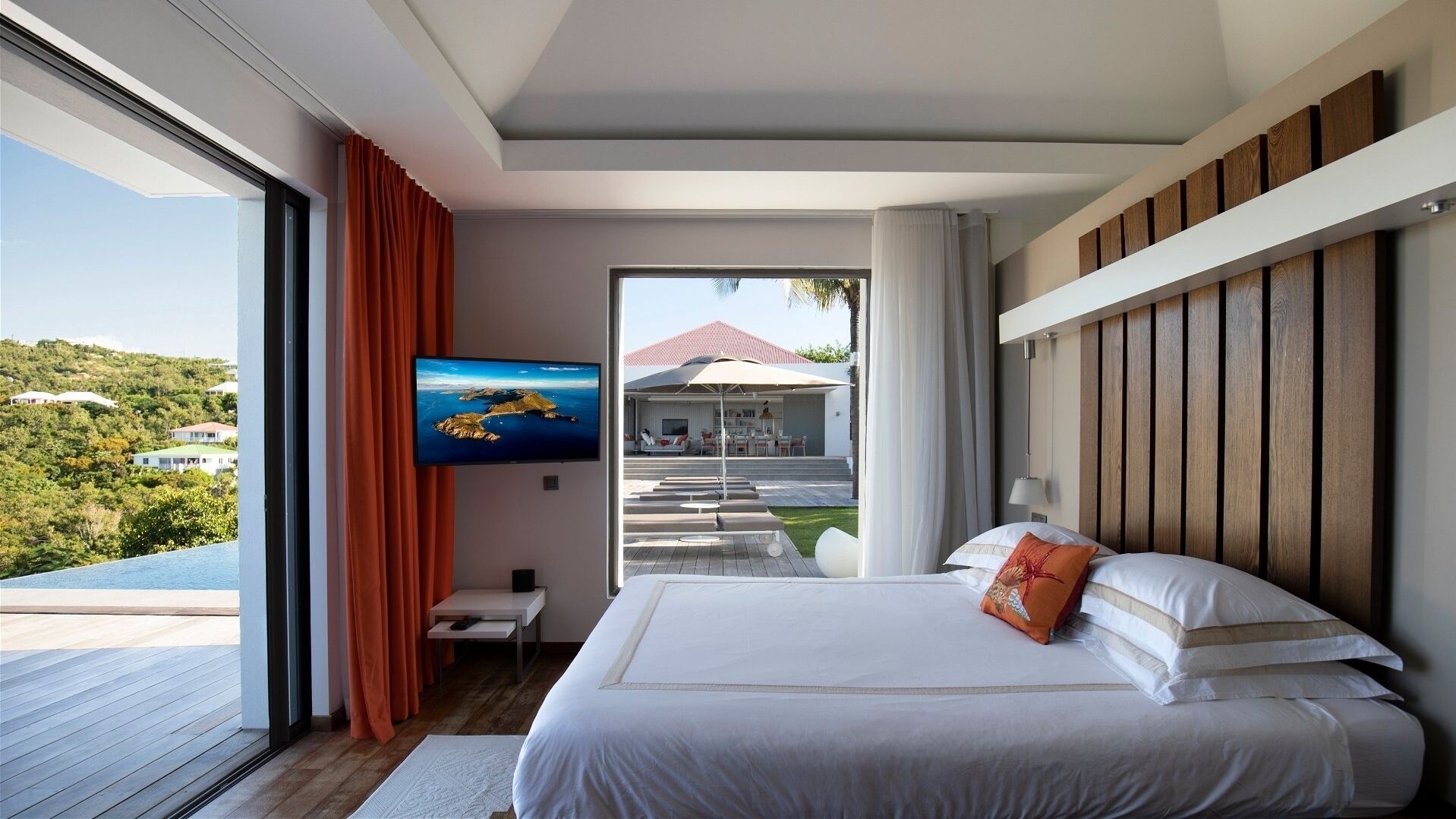Ein modernes Hotelzimmer mit einem großen Bett, einem an der Wand befestigten Fernseher und Blick auf den Außenpool und die Landschaft.