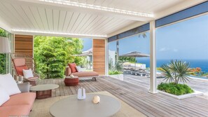 Un espace de détente extérieur moderne, doté d’une terrasse en bois, de sièges et offrant une vue sur l’océan.