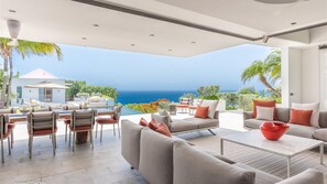 Un espace de vie extérieur moderne avec vue sur l’océan, comprenant un coin repas, des canapés et une table basse.