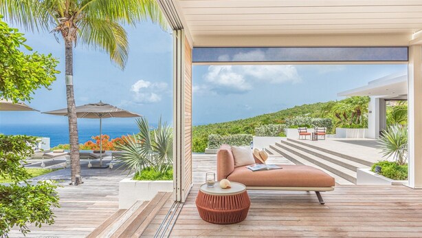 Ein moderner Außenbereich zum Entspannen mit Holzterrasse, bequemen Sitzgelegenheiten und Blick aufs Meer.