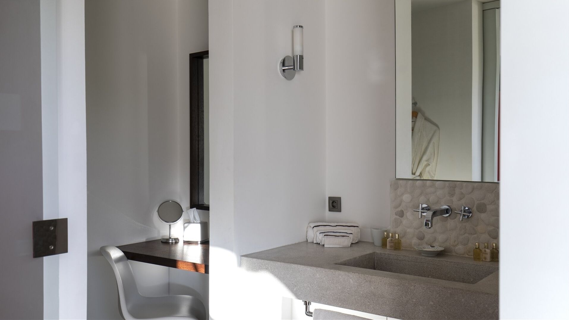 A modern bathroom with a large mirror, a round vanity, and a sink with a stone backsplash.