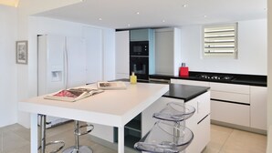 A modern kitchen with white cabinetry, a black countertop, and a small island with bar stools. - Belombre Luxury villa (Marigot)