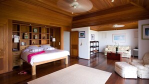 A spacious bedroom with a large bed, wooden shelving, and a cozy sitting area with a sofa and armchairs. - Manoir de Lurin Luxury villa (St Barths)