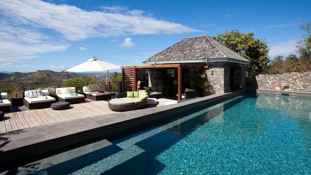A clear blue pool with a wooden deck and outdoor seating area. - Manoir de Lurin Luxury villa (St Barths)