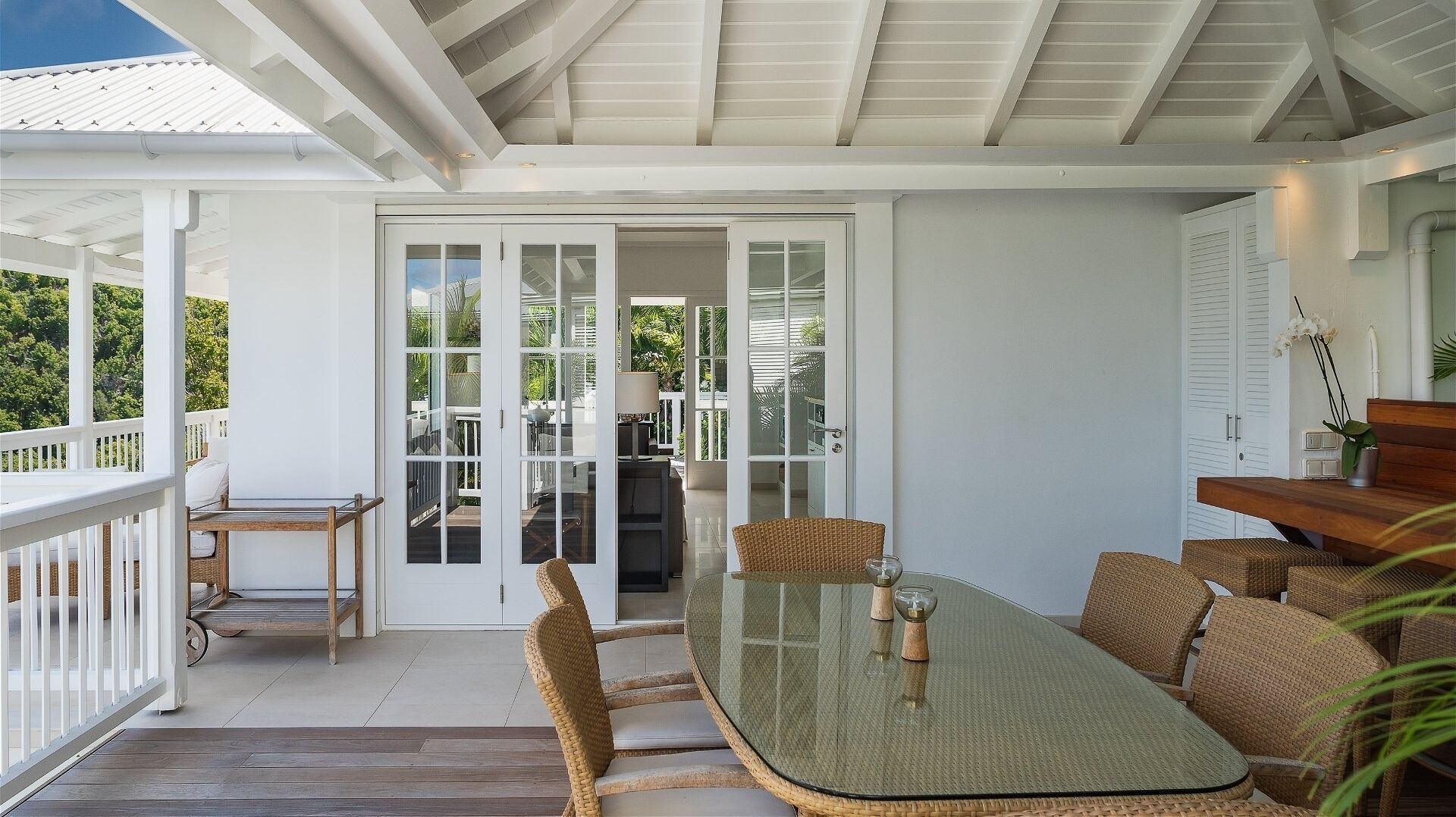 Un espace extérieur abrité, doté d’une porte vitrée donnant sur un patio, avec des meubles en osier et une table en bois.