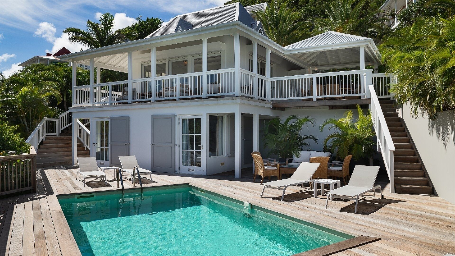 Una casa de dos pisos con piscina, muebles de exterior y una escalera que lleva a un balcón.