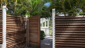 Una entrada protegida por un portón metálico y una puerta de madera, rodeada de abundante vegetación y un cielo despejado.