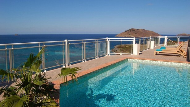 A pool with clear blue water, surrounded by a white railing, and overlooking a scenic ocean view with a distant island.