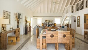 Un vaste espace de vie doté d’un haut plafond, d’un escalier et d’un coin repas aménagé avec des meubles en osier.