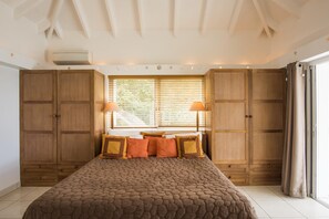 A bedroom with a large bed, wooden wardrobe, and a window with blinds.