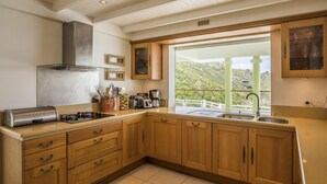 A kitchen with wooden cabinets, a stainless steel range hood, a window with a view of a mountainous landscape, and a countertop with various appliances. - Beautiful Ushuaia Luxury villa (Flamands)