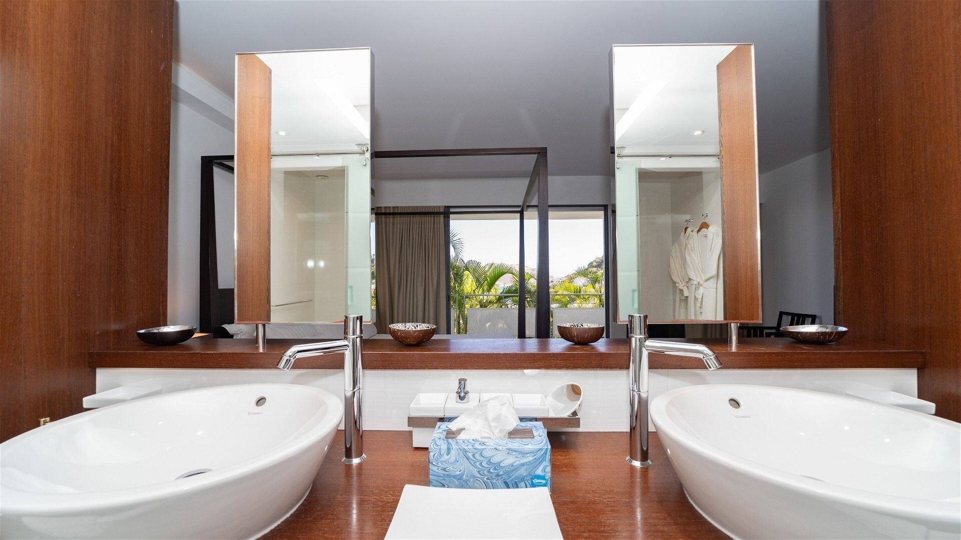 Une salle de bain moderne avec deux grands lavabos, un miroir et une vue sur un balcon agrémenté de plantes.