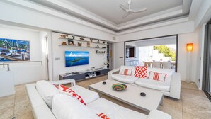 A modern living room with a white sofa set, a flat-screen TV, and a dining area visible through an open door. - Matajagui Luxury villa (Flamands)