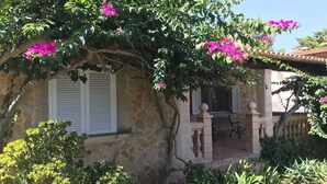 A stone building with a covered porch, white shutters, and pink flowering vines. - Villa de Bonaire, Alcudia, large garden + pool, close to the beach, WiFi, for 8 people (Alcudia/Bon Aire)
