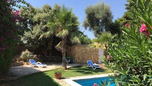 A backyard with a swimming pool, two lounge chairs, and various plants. - Villa de Bonaire, Alcudia, large garden + pool, close to the beach, WiFi, for 8 people (Alcudia/Bon Aire)