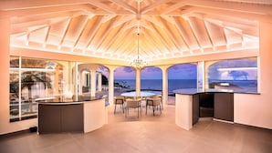 A spacious room with a large window overlooking the ocean, a central seating area, and a bar counter. - Byzance (1/2 Rooms) Luxury villa (St Barts)