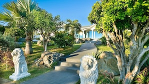 A pathway leading to a building with columns, surrounded by statues and lush greenery. - Byzance (1/2 Rooms) Luxury villa (St Barts)