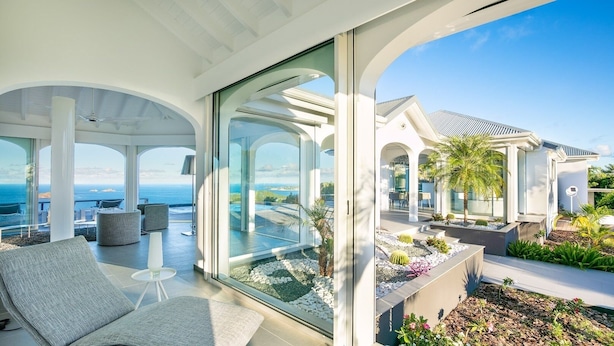 A modern, open-plan living area with a glass wall offering a view of the ocean and a landscaped outdoor area with cacti and plants. - Beautiful Byzance Luxury villa (St Barts)
