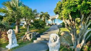 A pathway leading to a building with columns, surrounded by statues and lush greenery. - Beautiful Byzance Luxury villa (St Barts)