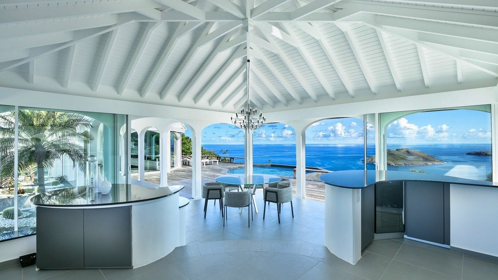 A modern kitchen with a view of the ocean, featuring a curved island, bar area, and a dining set.