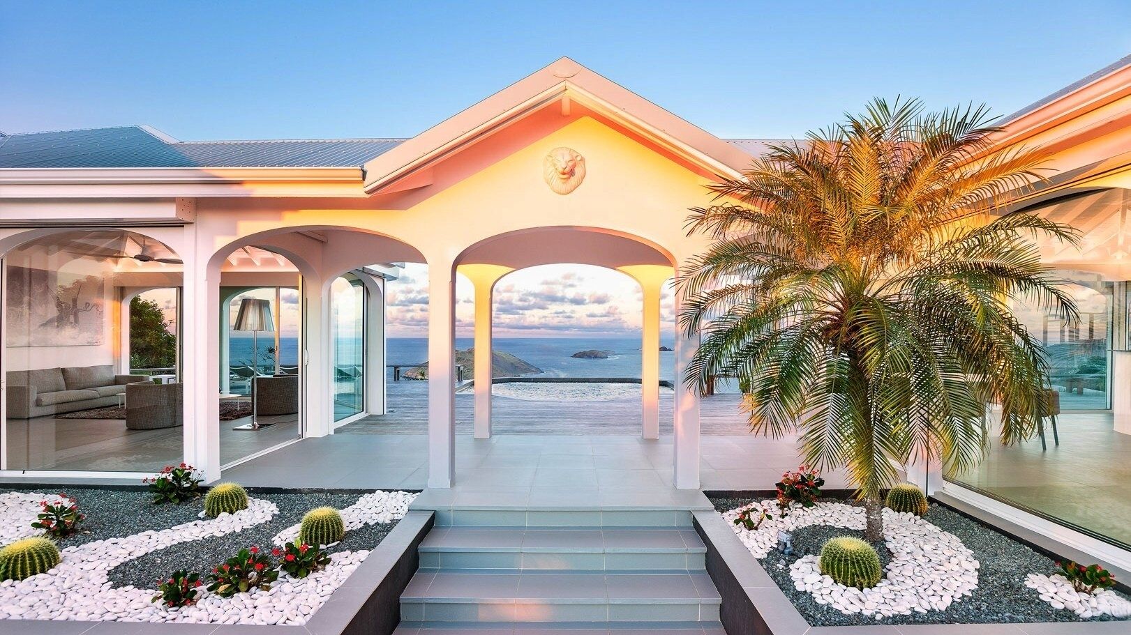 A modern house with a glass facade, a central archway, and a view of the ocean.