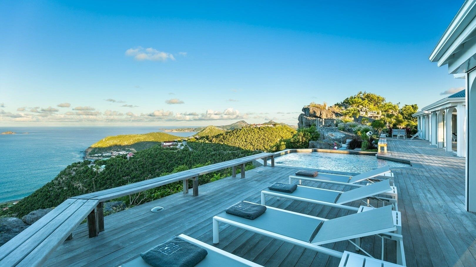 A wooden deck with lounge chairs overlooking a pool and ocean view.
