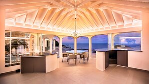 A spacious room with a large window overlooking the ocean, a central seating area, and a bar counter. - Beautiful Byzance Luxury villa (St Barts)