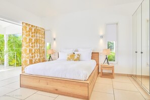 A modern bedroom with a wooden bed, white bedding, and a view of greenery outside.