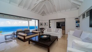Ein geräumiges Wohnzimmer mit großem Fenster zum Meerblick, ein weißes Sofa, ein Couchtisch und ein Bücherregal.