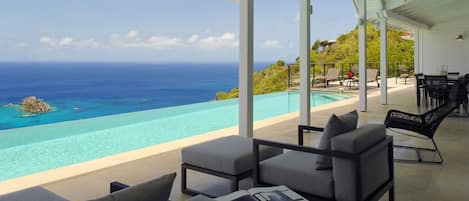 Un espace de détente extérieur moderne, doté d’une piscine donnant sur un océan d’un bleu profond et sur une île lointaine.