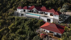 A modern villa with a swimming pool, multiple red-roofed structures, and lush greenery surrounding the property. - The View Luxury villa (St. Barthelemy)