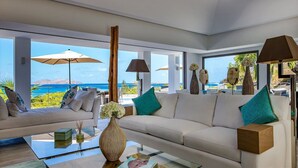 A modern living room with a large sofa, a coffee table, and a view of the ocean. - Avenstar (4/5 Rooms) Luxury villa (Camaruche)