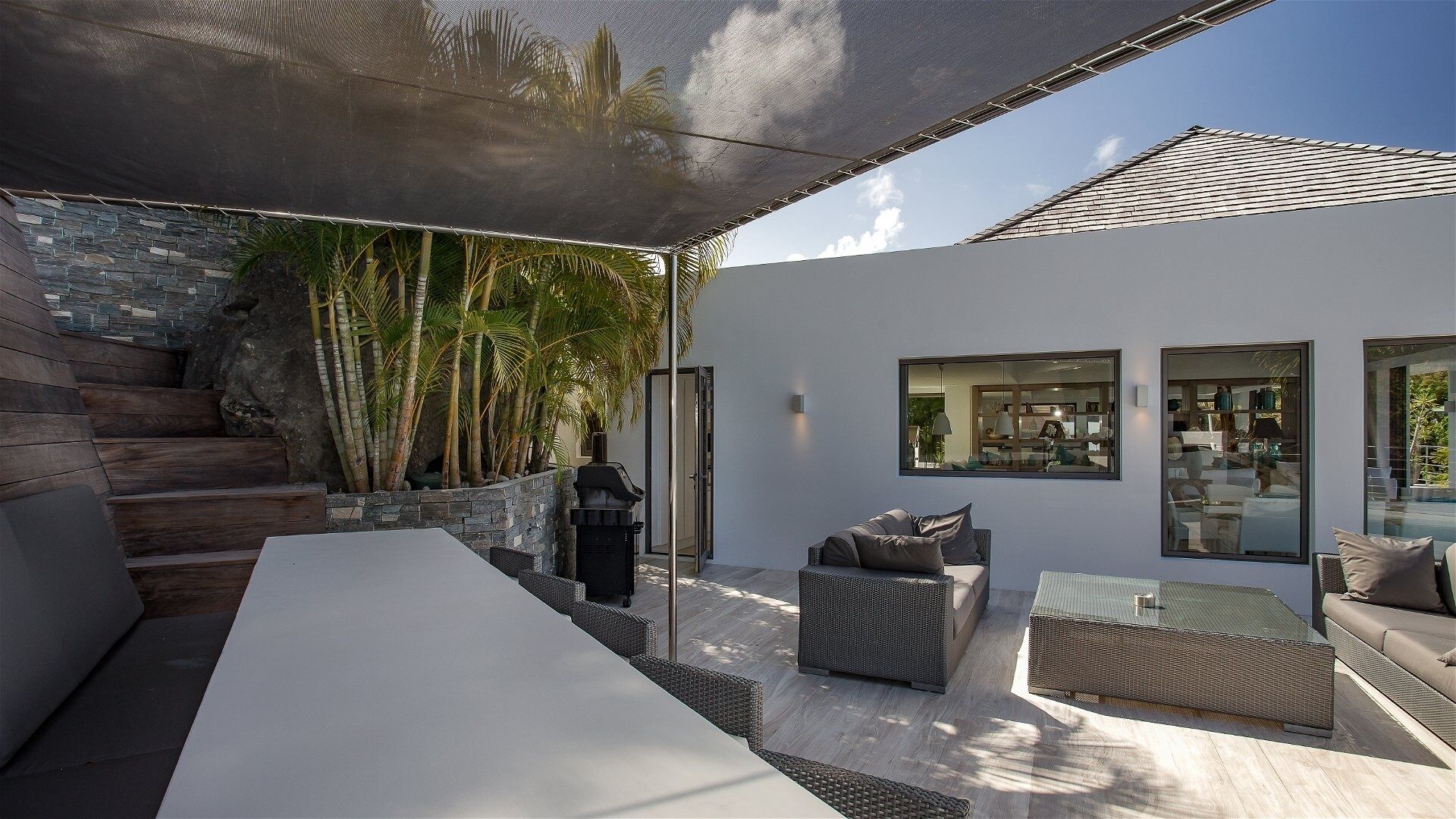 A modern outdoor living area with a stone wall, a grill, and a seating arrangement including a table and chairs.