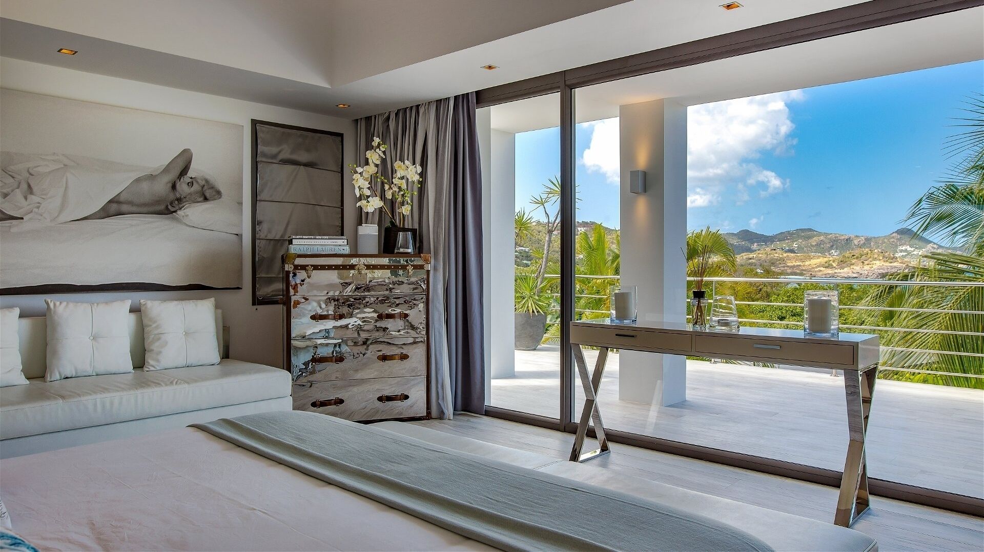 Une chambre à coucher moderne avec un grand lit, un canapé, une commode et une vue sur l’extérieur.