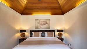 A bedroom with a wooden ceiling, a large bed with beige bedding, two wall-mounted lamps, and a turtle-themed artwork above the bed. - Captain Cook (1/4 Rooms) (Pointe Milou)