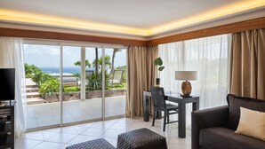 Camera d'albergo con un'ampia porta-finestra scorrevole che si apre su un balcone con vista sull'oceano. All'interno, un divano dai toni scuri, un tavolino con una lampada e una TV su un mobile.