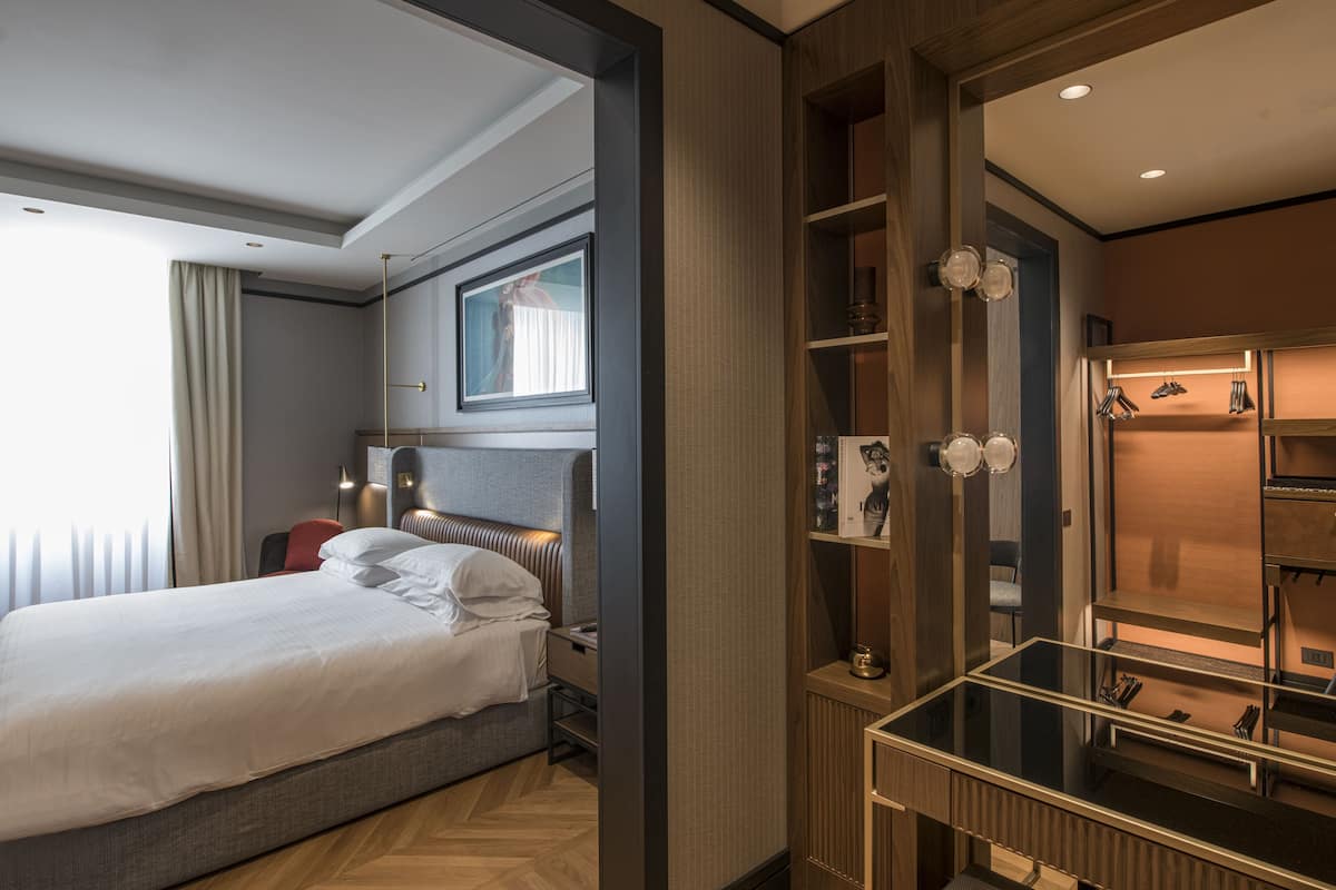 Een moderne hotelkamer met een groot bed, een bureau met een glazen blad en een inbouwkast.