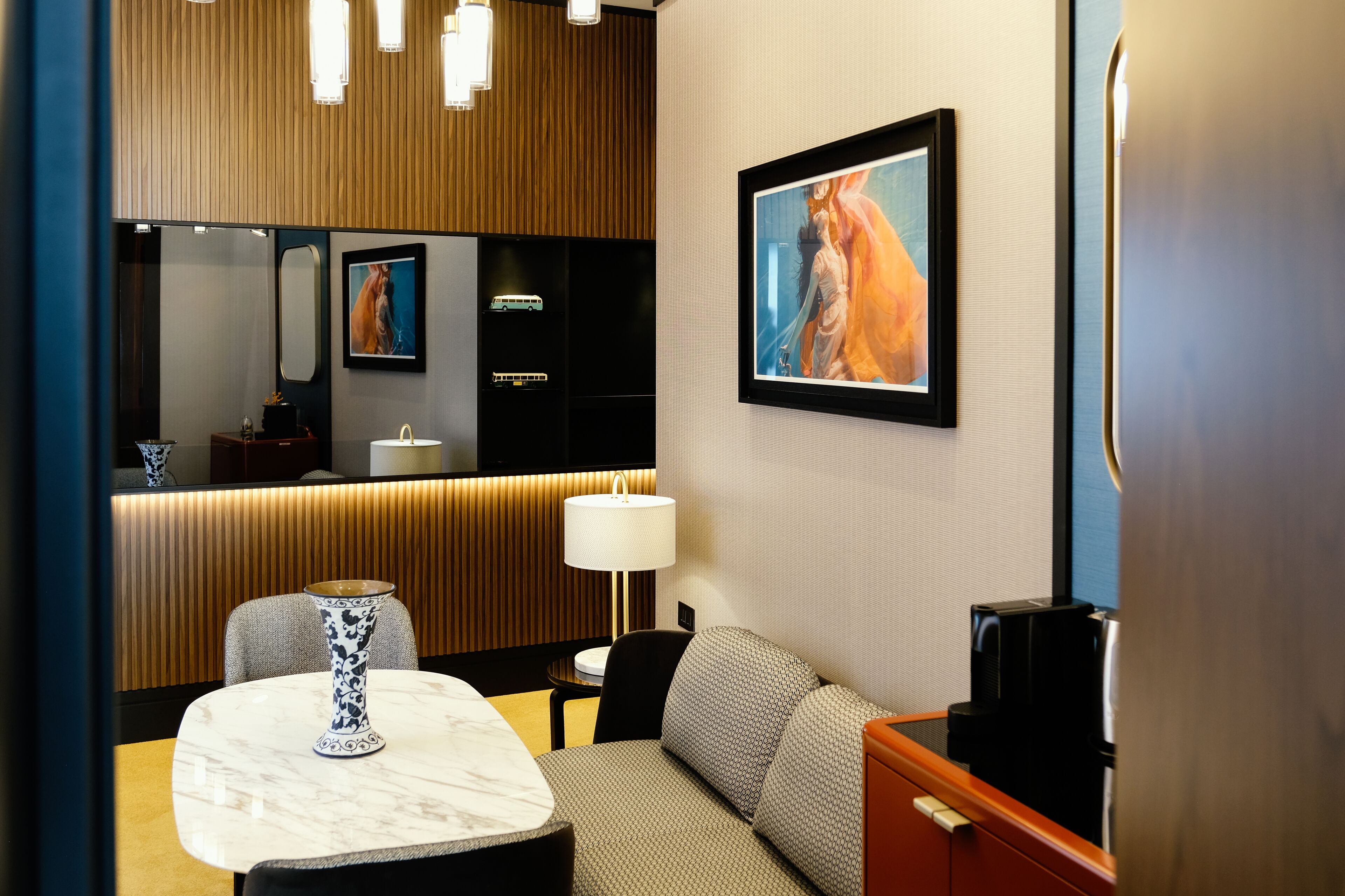 Quarto de hotel com parede de painel de madeira, um espelho grande, uma obra de arte emoldurada, um sofá, uma mesa com um vaso e uma cafeteira.