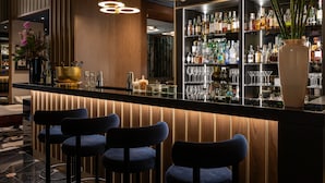 A bar area with a wooden bar counter, blue bar stools, and a well-stocked liquor shelf.