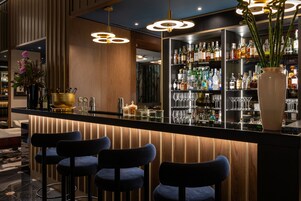 Zona de bar con mostrador de madera, taburetes azules y una estantería bien surtida de licores.