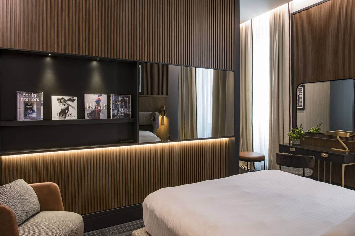 Een moderne hotelkamer met een groot bed, een bureau met een spiegel en een wandplank met ingelijste foto's.