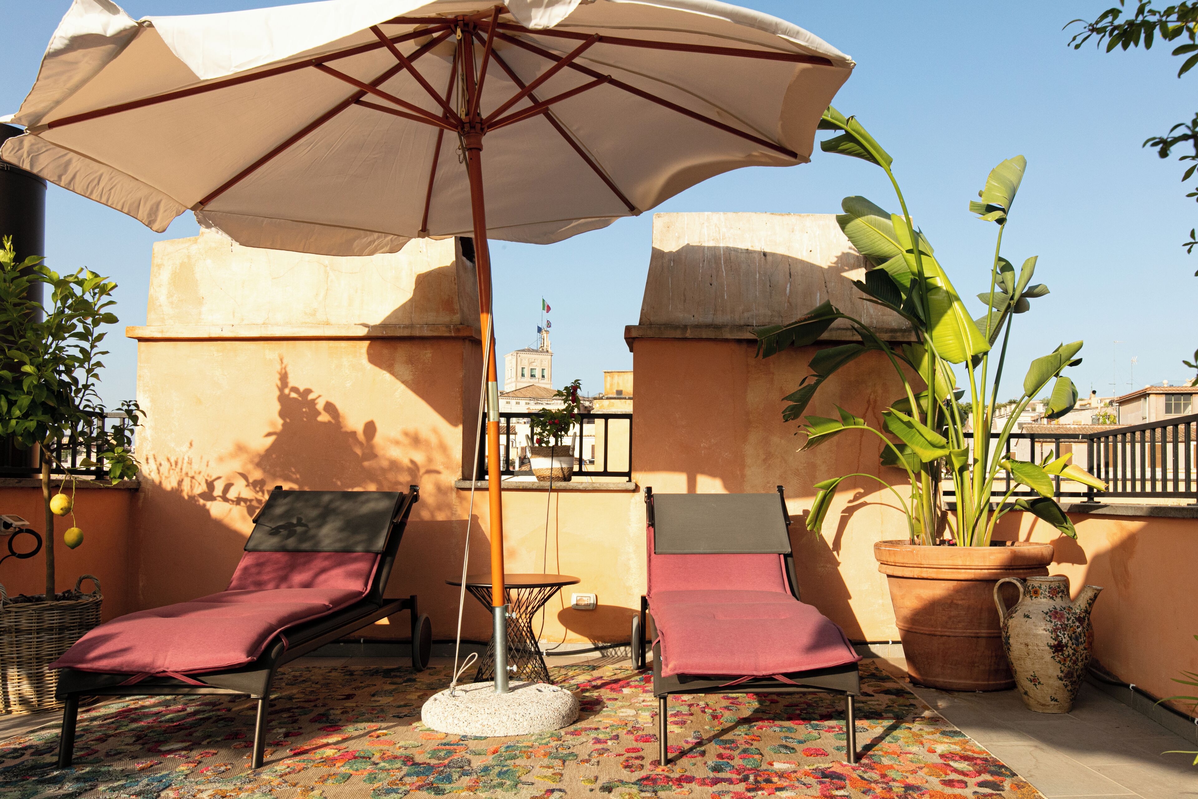 A terrace with two lounge chairs, a large umbrella, a potted plant, and a decorative vase.